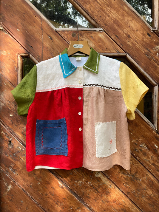 Short-sleeved shirt made from a patchwork of multicoloured vintage linen napkins. Shown hanging on a wooden door