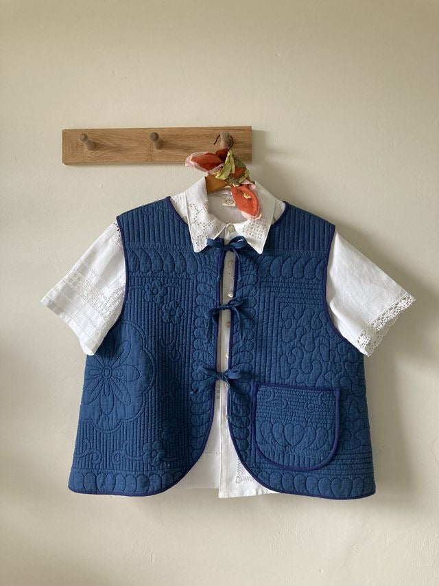 Blue gilet/bodywarmer/waistcoat made from a recycled quilt. It has a tie front and is shown over a white shirt
