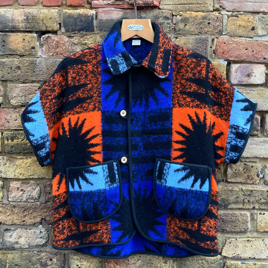 Crop-sleeved jacket made from a fabulous reclaimed blanket with starburst motifs in bright blue, light blue, black and orange, hanging against a brick wall